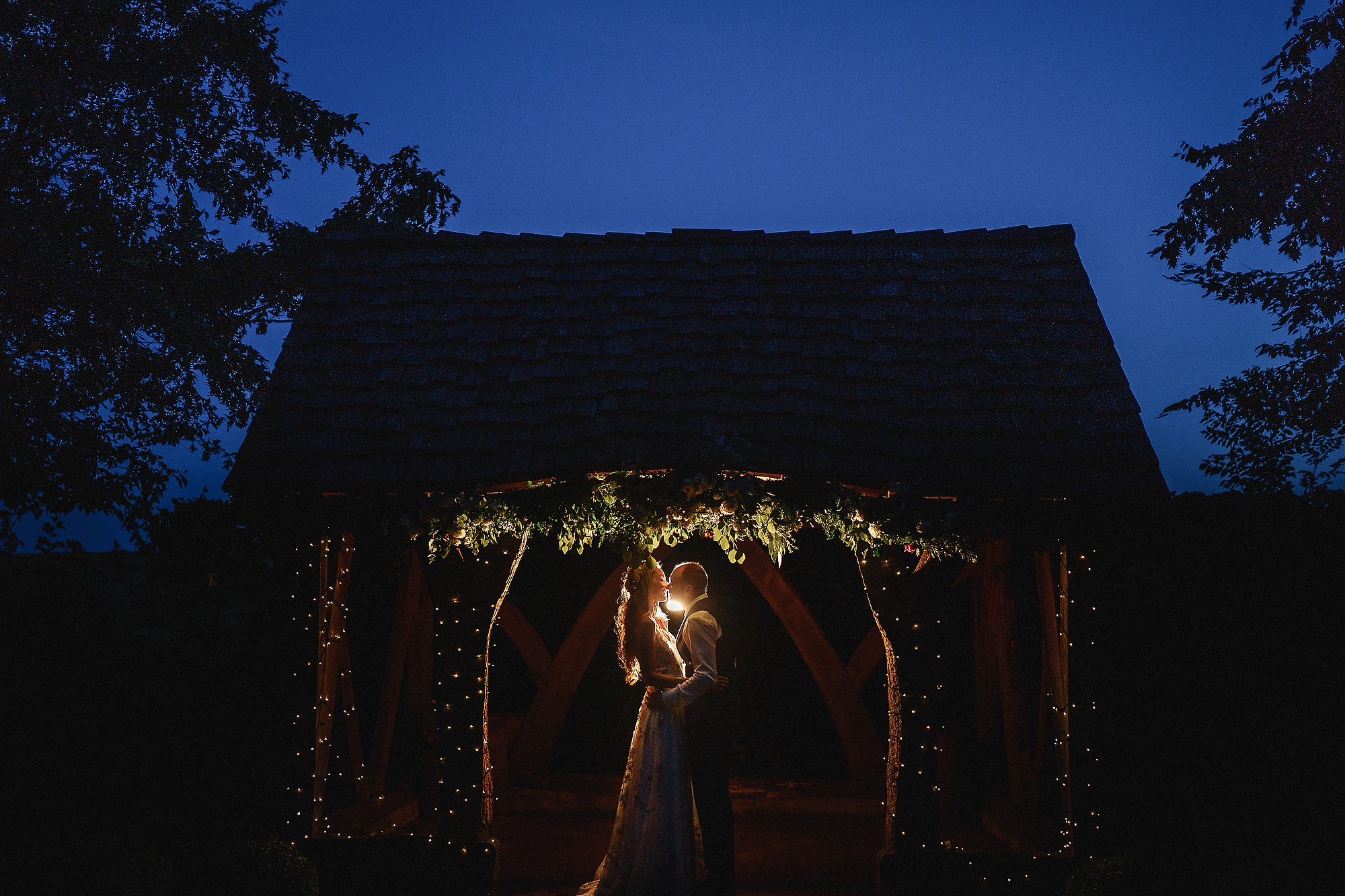 Wedding couple kissing at wedding in front of the oak beams outside at Cripps Barn